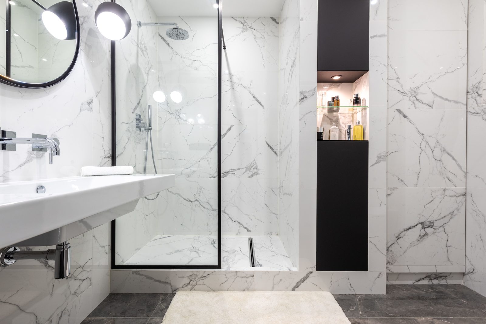 Custom black-framed glass shower panel against book-matched marble tile, fabricated by Makibaki near Deerfield, IL