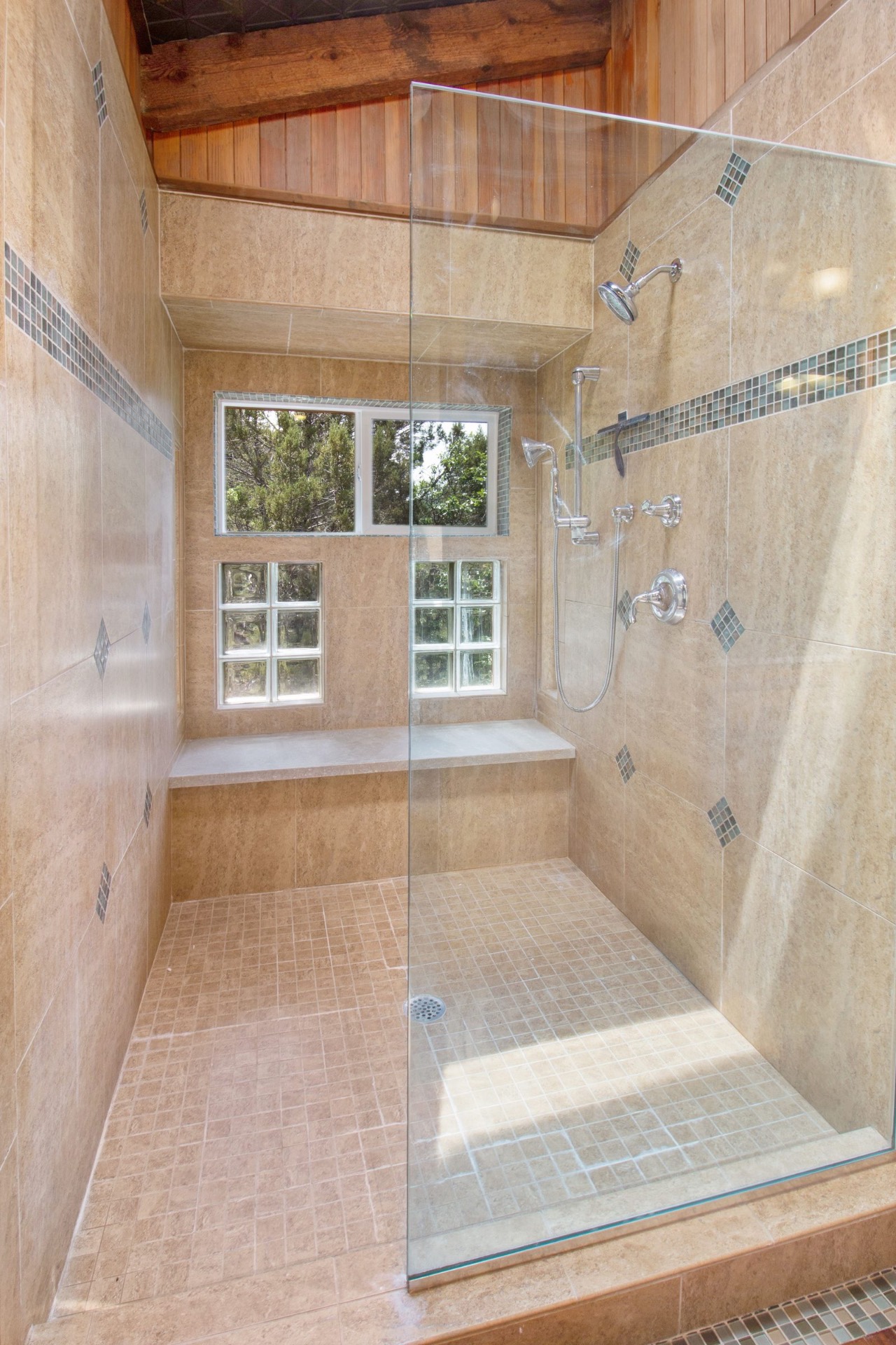 Frameless travertine walk-in shower with glass panel and built-in bench, installed by Makibaki near Deerfield, IL