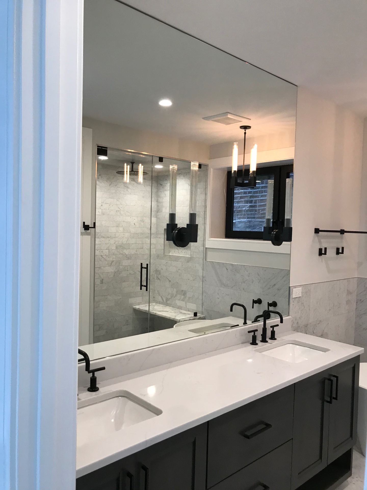 Large frameless vanity mirror over double sinks in a Carrara marble bathroom, by Makibaki